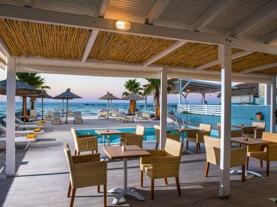 Area ristorante all'aperto sulla spiaggia con vista sulla piscina e sul mare sullo sfondo.