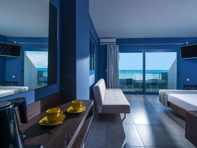 Camera d'hotel moderna con vista mare, pareti blu e balcone con ringhiera in vetro.