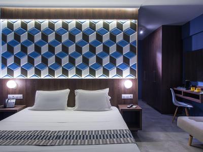 Camera d'hotel moderna con letto grande, testiera geometrica e area scrivania.