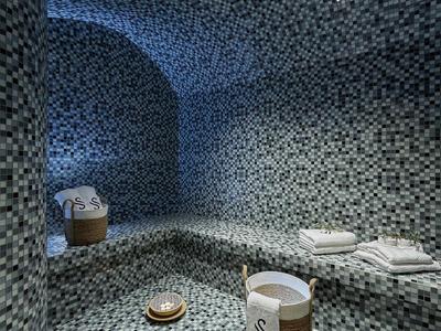 Nowoczesna łaźnia parowa z mozaikowymi płytkami w chłodnych odcieniach niebieskiego i białymi ręcznikami.