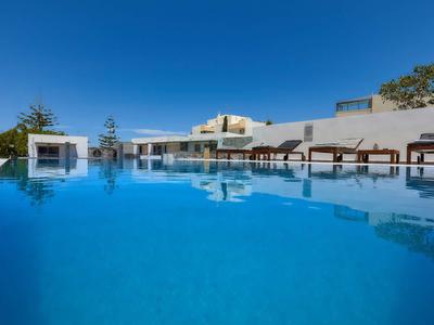 Piscina moderna con lettini e acqua azzurra limpida sotto un cielo blu in un hotel.