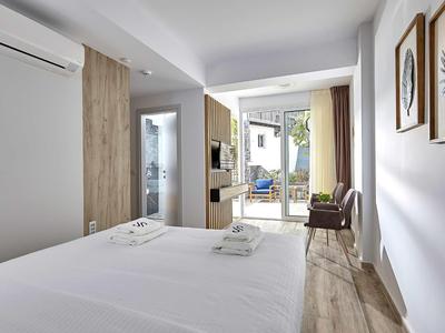 Camera d'hotel moderna con letto matrimoniale, area salotto e accesso a un balcone con vista sul mare.