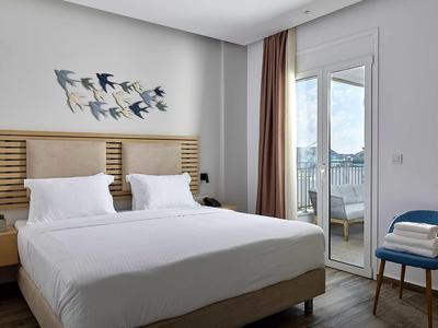 Nowoczesny pokój hotelowy z podwójnym łóżkiem, dekoracją ścienną z ptaków i balkonem z widokiem na morze.