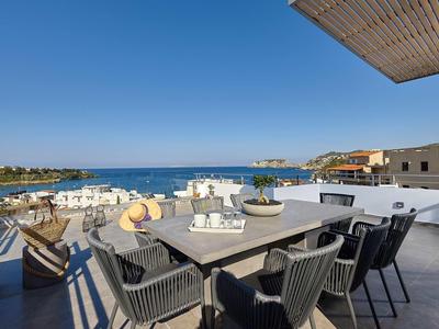 Terrazza con tavolo da pranzo moderno e sedie con vista sul mare blu e cielo sereno.