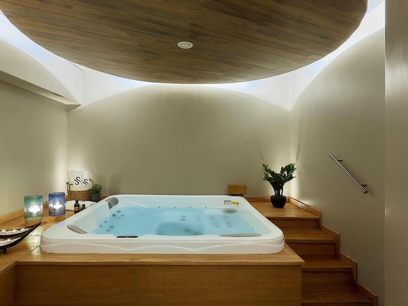 Nowoczesna łazienka z podświetlanym jacuzzi, drewnianymi panelami i nastrojowym oświetleniem.