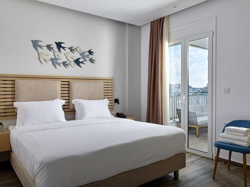 Nowoczesny pokój hotelowy z podwójnym łóżkiem, dekoracją ścienną z ptaków i balkonem z widokiem na morze.