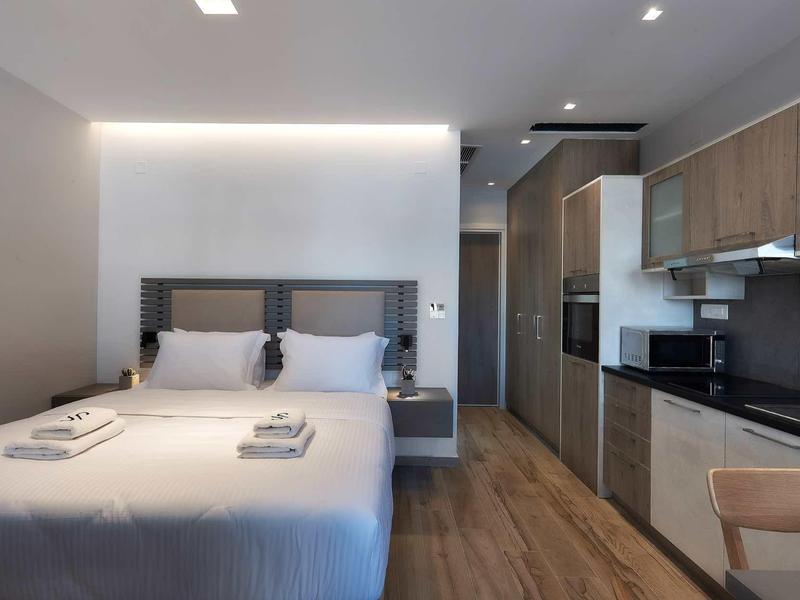 Nowoczesny pokój hotelowy z podwójnym łóżkiem i aneksem kuchennym w neutralnych kolorach.