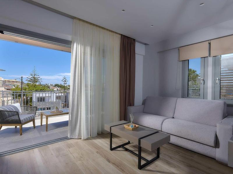 Nowoczesna część pokoju hotelowego z sofą, stołem i balkonem z krzesłami z widokiem na zewnątrz.