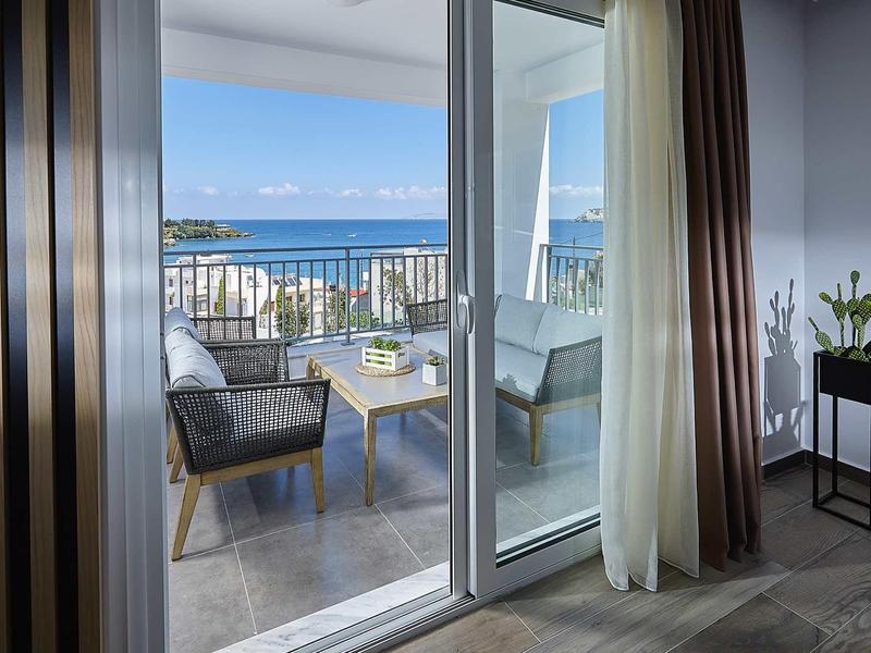 Balkon z krzesłami i stołem, widok na morze z pokoju hotelowego.