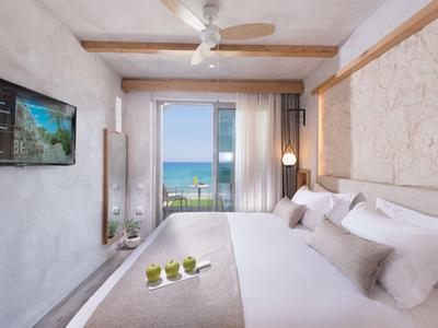 Modern hotelkamer met groot bed, zeezicht en plafondventilator.