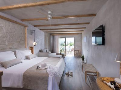 Hell eingerichtetes Schlafzimmer mit Doppelbett, Holzbalken, Balkon und modernem Fernseher an der Wand.