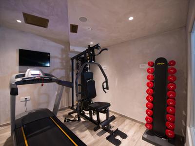 Kleiner Fitnessraum mit Laufband, Kraftstation, roten Hanteln und hellen Wänden und Boden.
