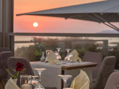 Tisch im Restaurant mit eingedeckten Gläsern, Servietten und Blick auf Sonnenuntergang am Meer.
