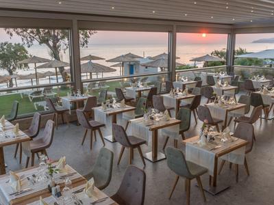 Elegantes Restaurant mit gedeckten Tischen, Blick auf Garten und Sonnenuntergang am Meer.