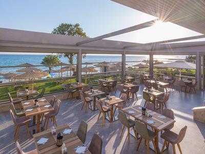 Zonnig terras met tafels en zeezicht bij een hotelrestaurant.
