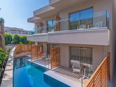 Modern hotel complex with pool and balconies, surrounded by wooden railings and blue sky.