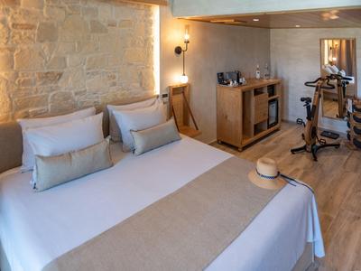 Gemütliches Schlafzimmer mit Doppelbett, Steinwand, Holzfußboden und antikem Fitnessgerät.