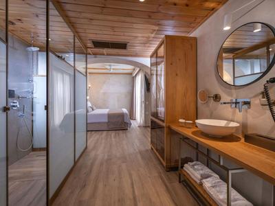 Modern hotel room with wooden floor, spacious wash area, and cozy bed in the background.