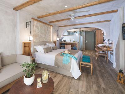 Bright modern hotel room with wooden beams, double bed, sofa, and dining table.