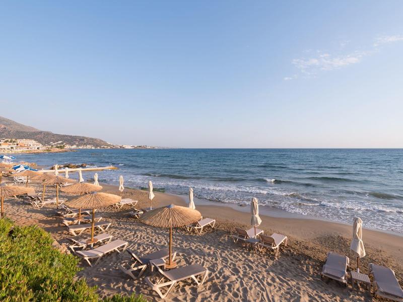 Ligbedden en parasols op een zandstrand naast een kalme zee onder een heldere lucht.