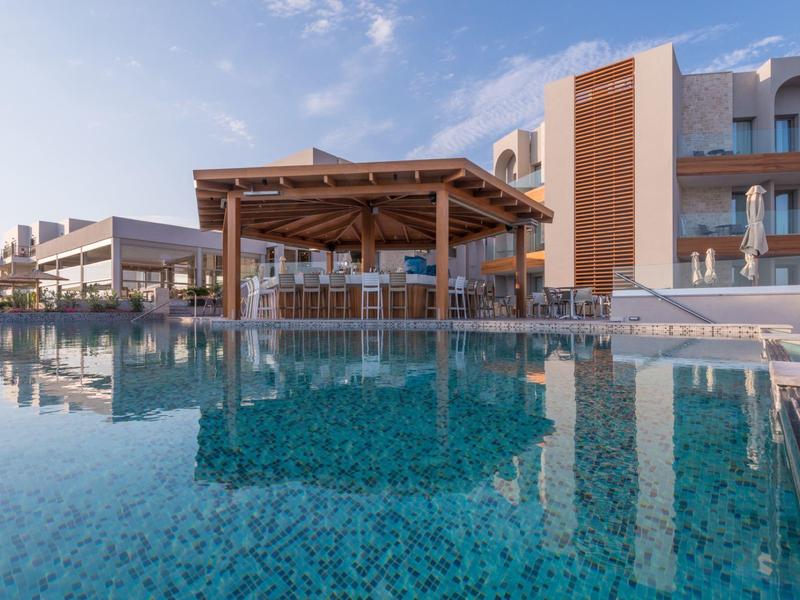 Zonnig hotelzwembad met houten pergola en modern gebouw weerspiegeld in water.