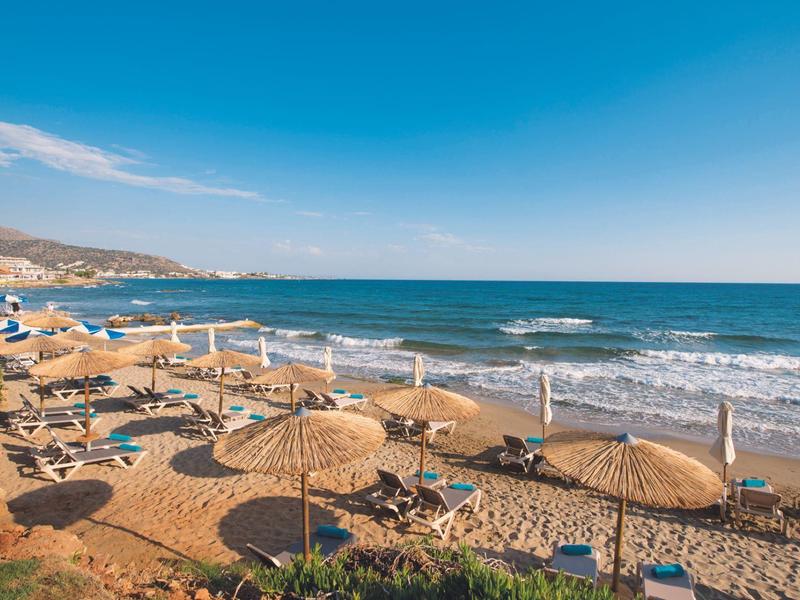 Zonnig strand met parasols en ligstoelen bij zee onder een heldere blauwe lucht.