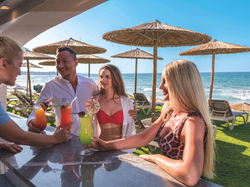 Groep vrienden die drinken genieten bij een strandbar met uitzicht op zee en parasols.