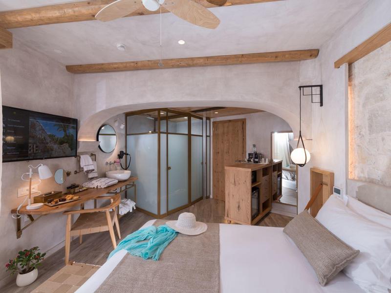 Gezellige slaapkamer met rustieke inrichting, houten balken, zitgedeelte en badkamer achter glazen deuren.