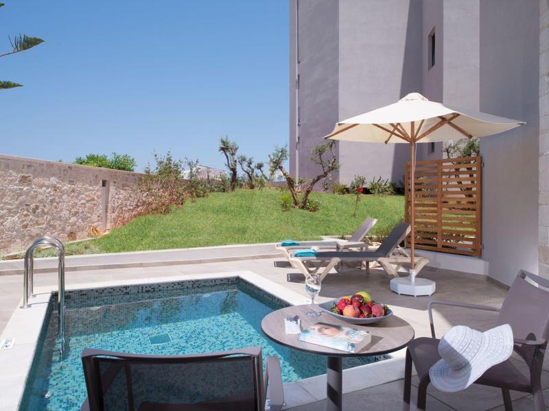 Buitenzwembad naast een terras met ligstoelen en parasol bij een modern gebouw.