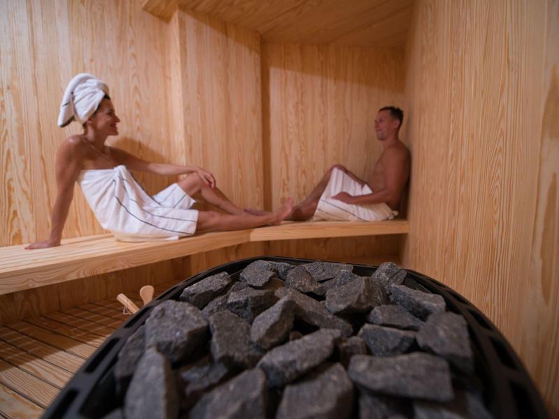 Twee mensen ontspannen in een houten sauna met een verwarming en stenen op de voorgrond.