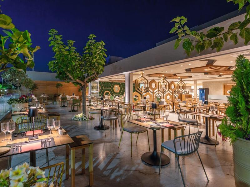 Buitenterras van restaurant 's nachts met tafels, stoelen en bomen onder donkere lucht.