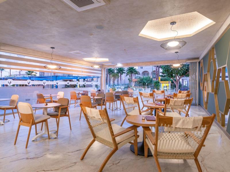 Moderne binnenrestaurant met houten tafels en stoelen, uitzicht op palmbomen buiten.