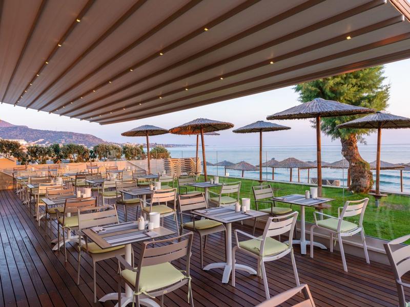 Buiten zitgedeelte met tafels, stoelen, parasols en uitzicht op water onder een overdekt terras.