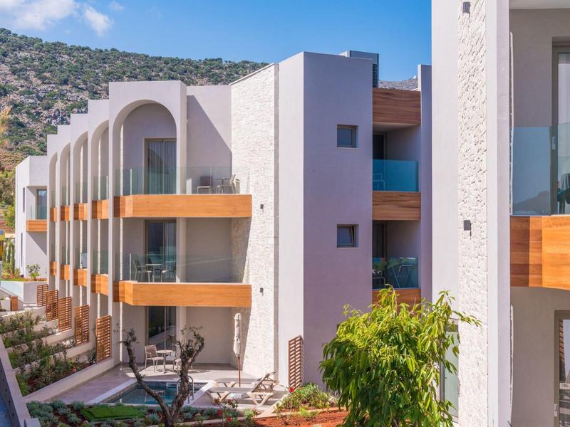 Modern hotel met balkons, houten leuningen en een berglandschap onder een heldere lucht.