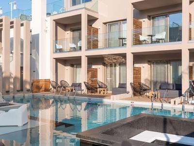 Piscina moderna de hotel con tumbonas y balcones de vidrio al atardecer.