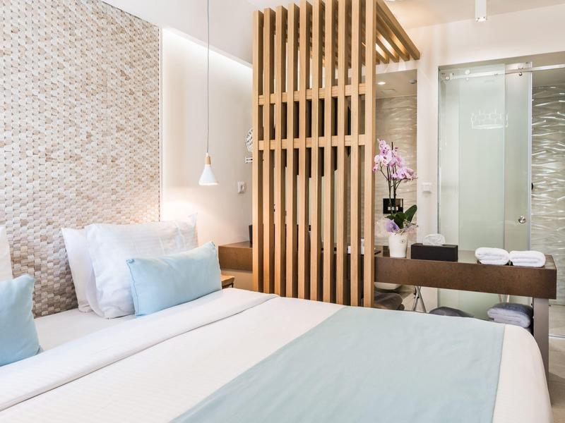 Jasny pokój hotelowy z dużym łóżkiem, drewnianą przegrodą i nowoczesną łazienką w tle.