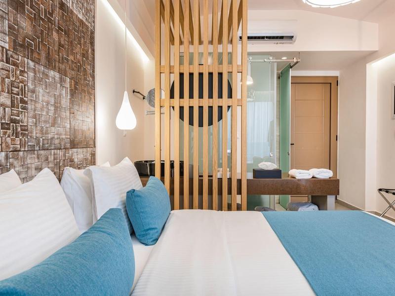 Nowoczesny pokój hotelowy z dużym łóżkiem, drewnianą przegrodą i łazienką w tle.