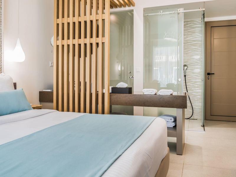 Nowoczesny pokój hotelowy z łóżkiem podwójnym, drewnianą ścianką działową i stylową jasną dekoracją.