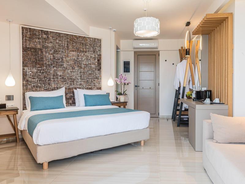 Nowoczesny pokój hotelowy z podwójnym łóżkiem, częścią wypoczynkową i minimalistycznym wystrojem.