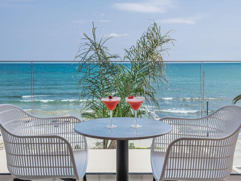 Dwa napoje na stole na tarasie z widokiem na morze i dwa krzesła.