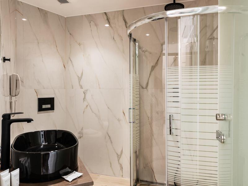 Nowoczesna łazienka z czarną wanną i przeszkloną kabiną prysznicową na tle marmurowej ściany