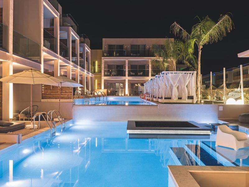 Nocny widok oświetlonego basenu hotelowego z leżakami i nowoczesną architekturą.