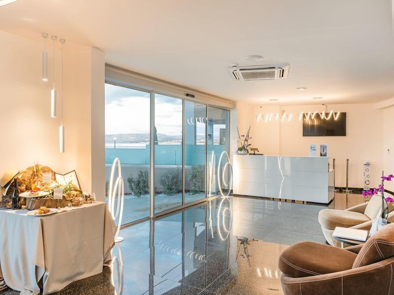 Jasna lobby hotelowa z błyszczącą podłogą, miejscem do siedzenia i dużym oknem z widokiem na morze.