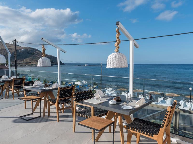 Taras restauracji z krzesłami i stołami z widokiem na morze i częściowo zachmurzone niebo.