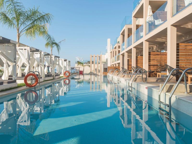 Nowoczesny basen na zewnątrz z leżakami i parasolami obok budynku hotelowego przy pogodnej pogodzie