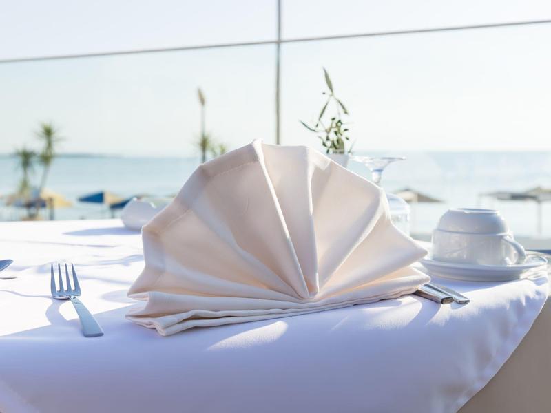 Eleganckie nakrycie stołu z złożoną serwetką wachlarzem przy oknie z widokiem na morze.