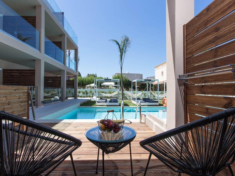 Widok z tarasu z dwoma krzesłami i stołem na basen i nowoczesne budynki hotelowe.