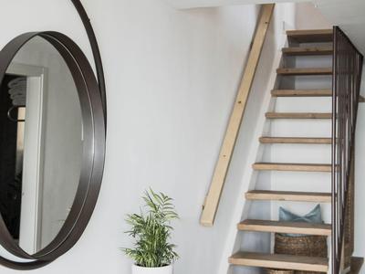 Ingresso moderno con scala in legno, specchio rotondo, pianta e libri.