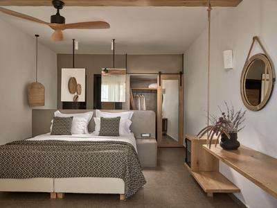 Camera d'hotel moderna con letto matrimoniale, ventilatore a soffitto, specchio e arredamento minimalista.