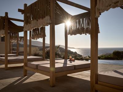 Camastros de madera con sombra junto a la piscina con vistas al mar al atardecer.